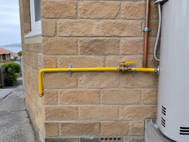 Yellow gas pipe and fittings on a brick exterior wall beside a gas unit in Bronte